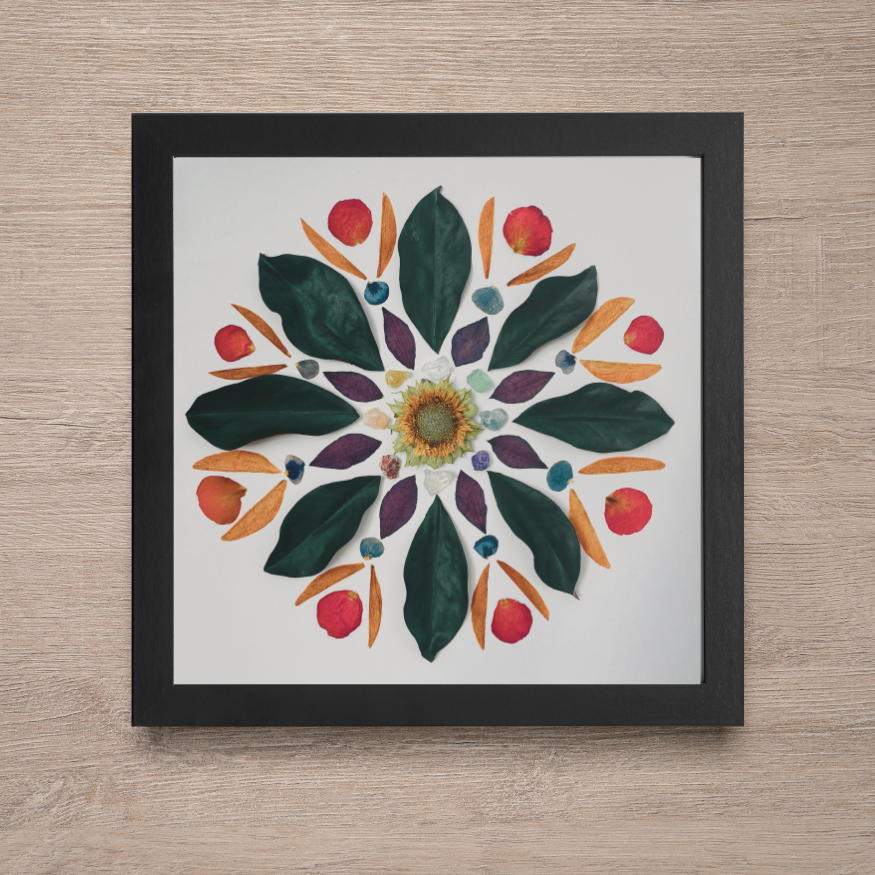 a nature mandala that is in a black frame, laying on a piece light beige colored wood.
